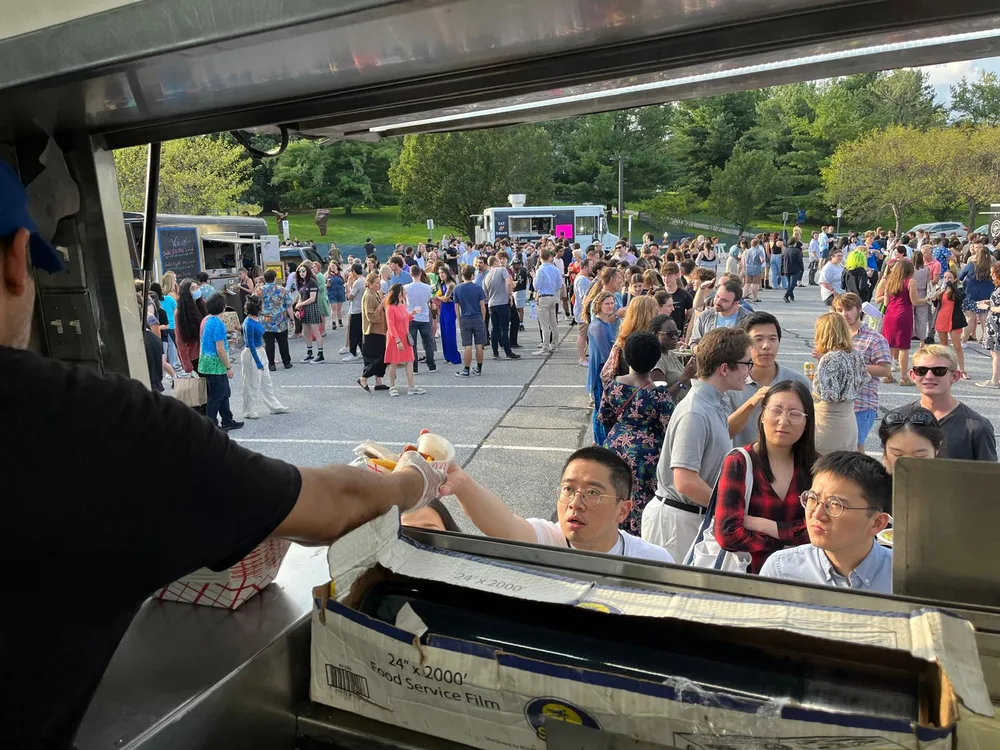 A crew member handing an order out of the truck window to a crowd at a campus event